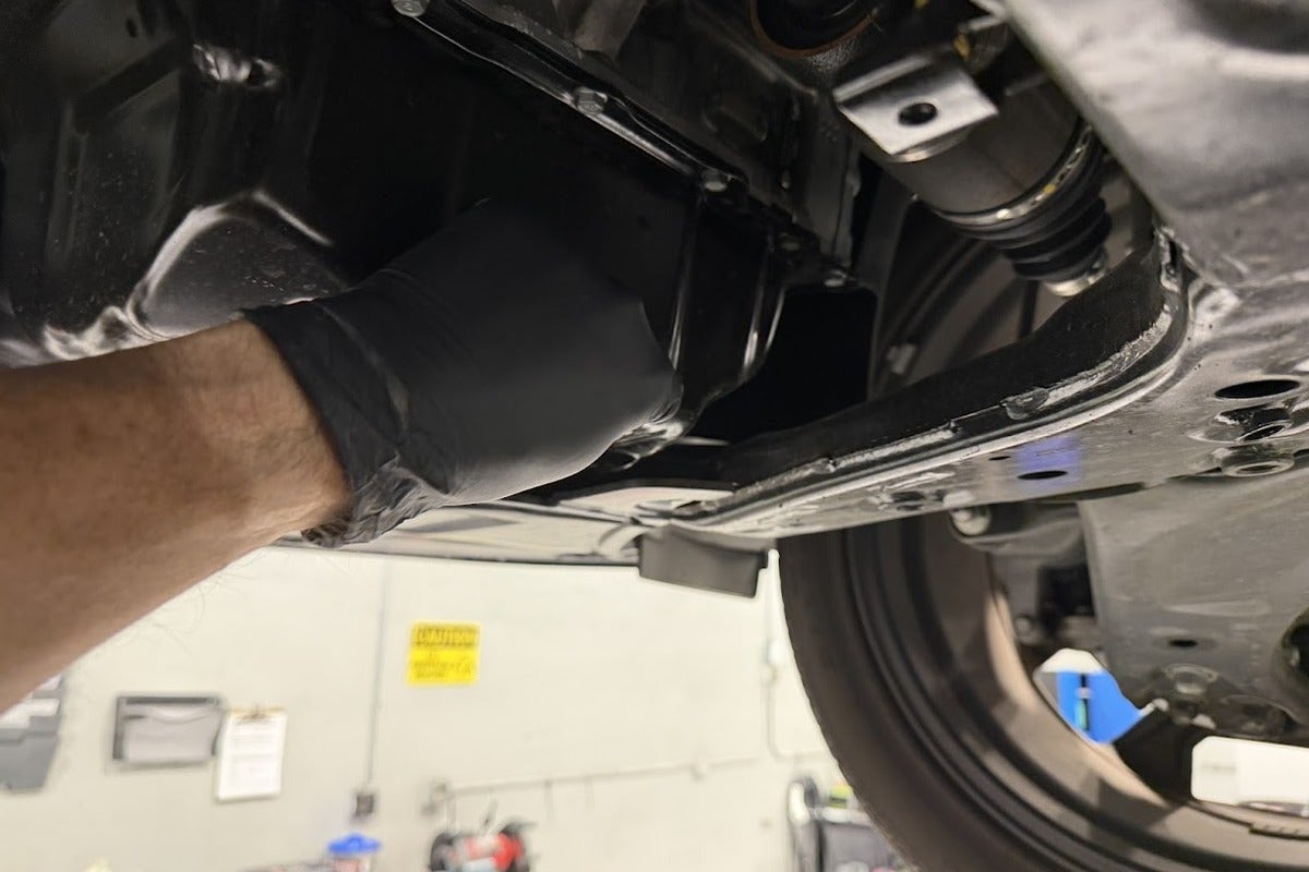 Technician performing an underbody maintenance inspection on a Kia at Kia of Portland
